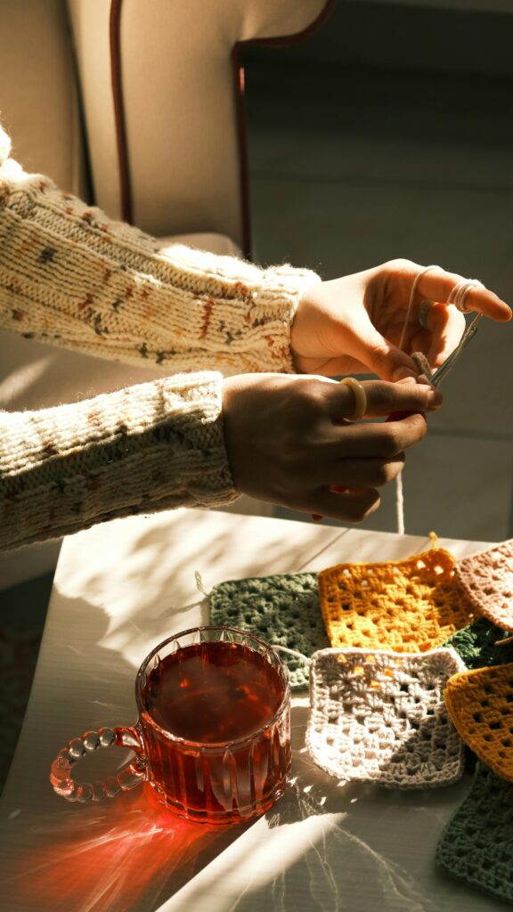 Warm sunlight highlights knitting hands and tea on a table, creating a cozy atmosphere.